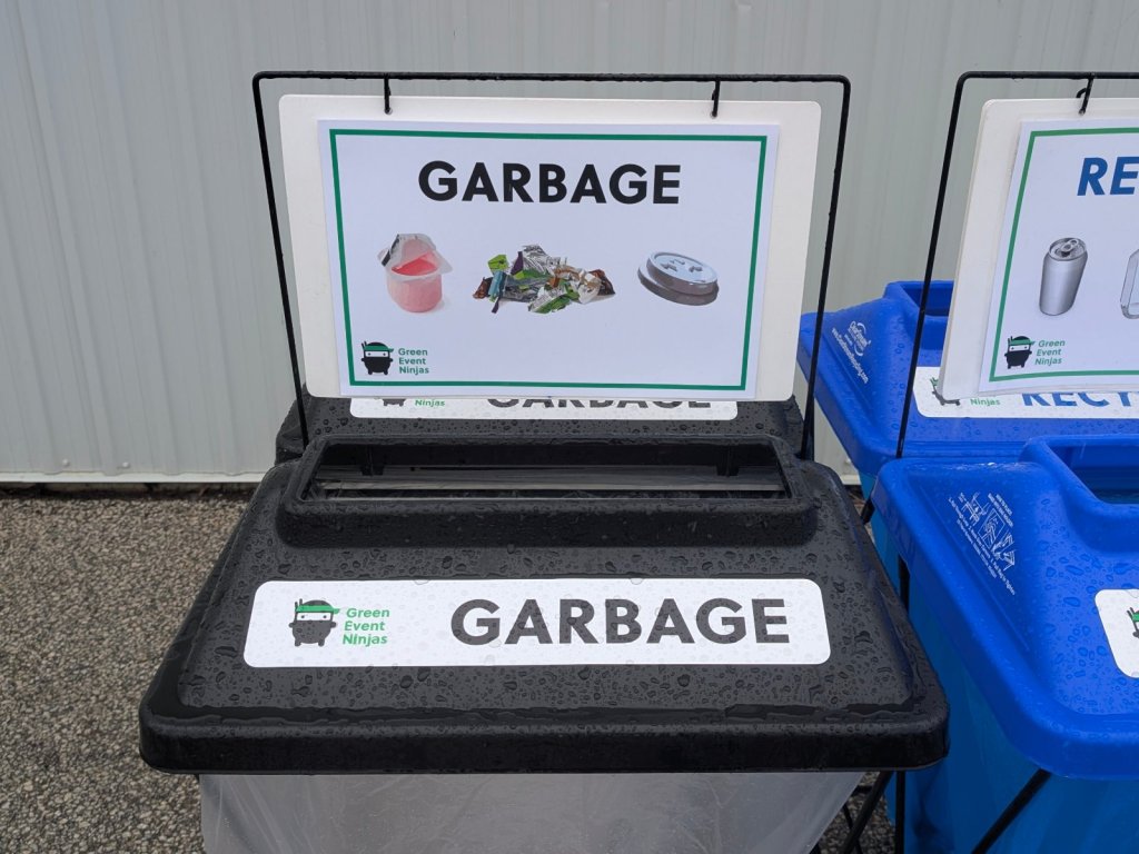 Close-up of an event garbage bin lid with a Green Event Ninjas label and a what-goes-where sign